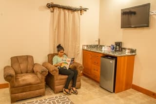 A woman sits in a plush chair reading a magazine in a softly lit room with a kitchenette.