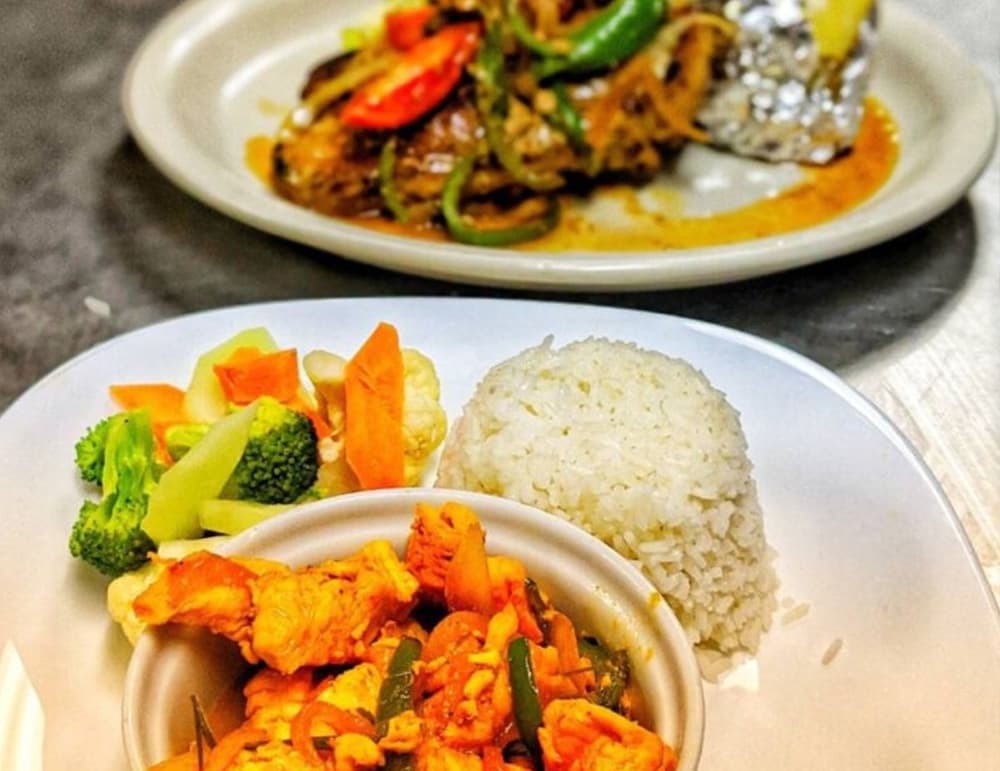 A plate of diced chicken stir-fry with vegetables, rice, and a second dish of meat and veggies in the background.