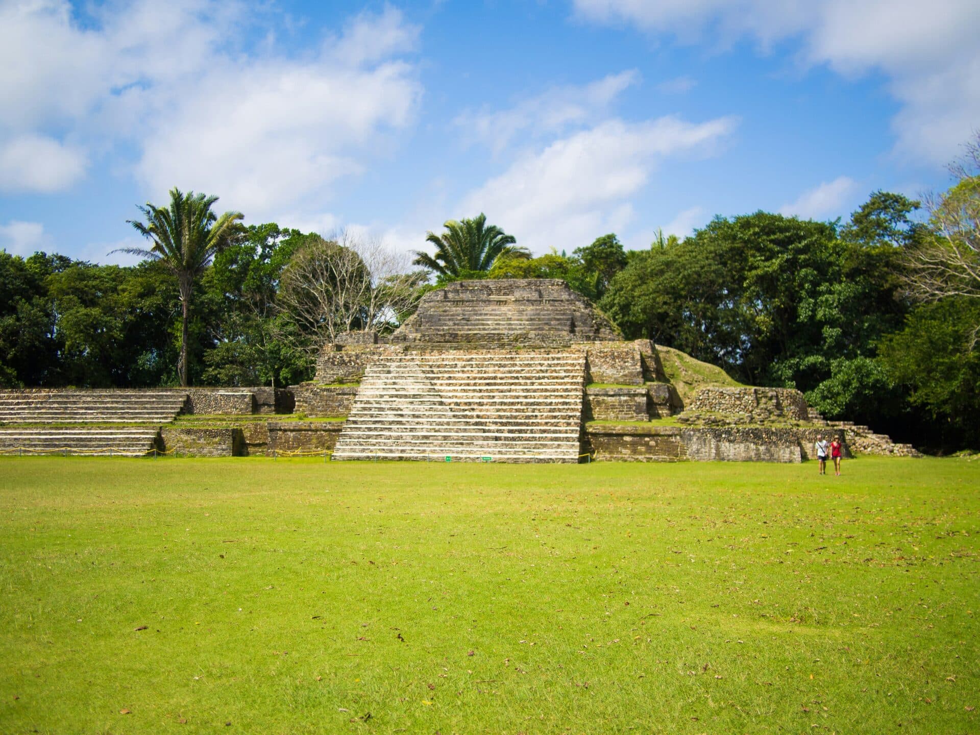 Ancient stone pyramid surrounded by lush greenery under a bright blue sky.