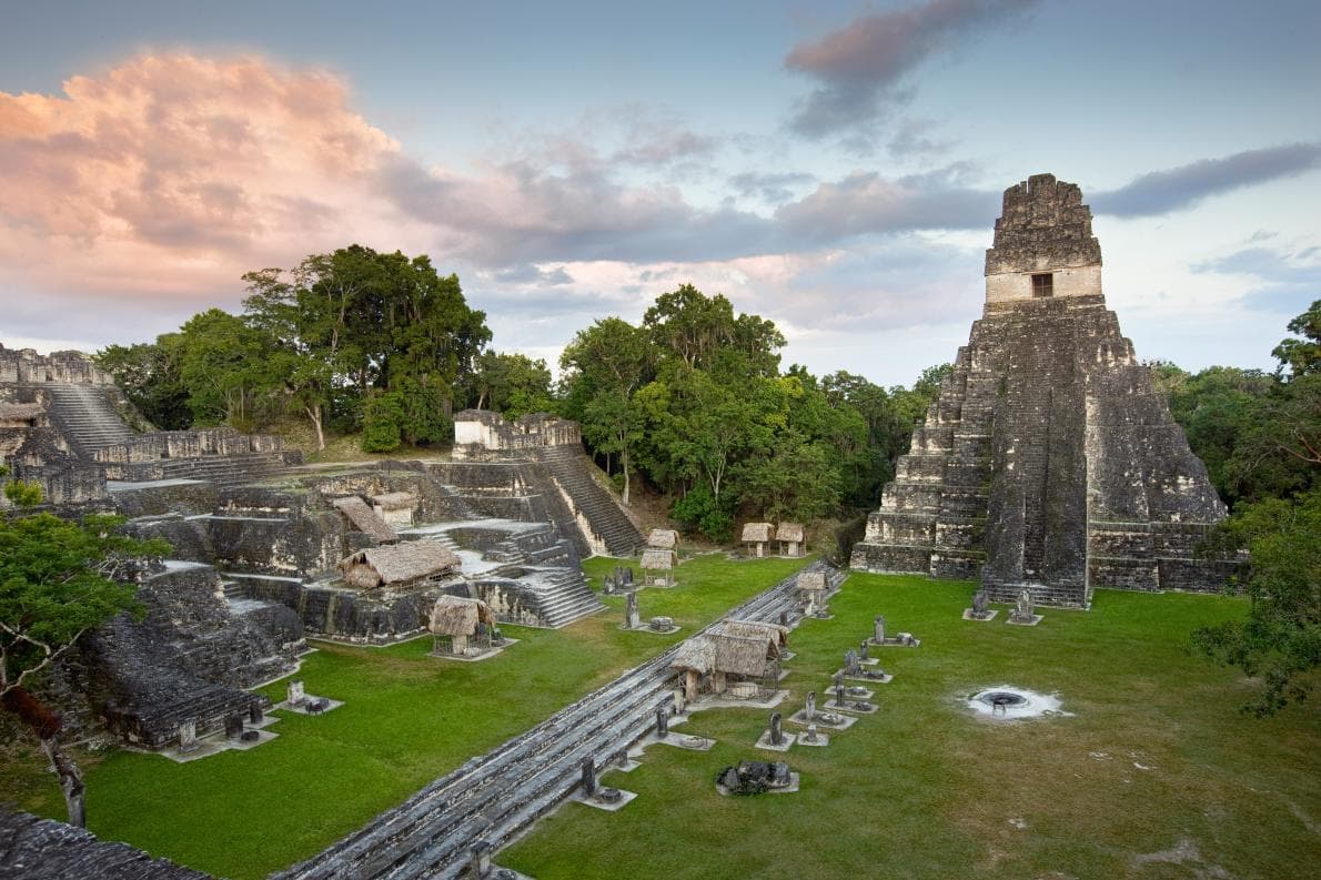 An ancient Mayan temple complex surrounded by lush greenery under a colorful sky.