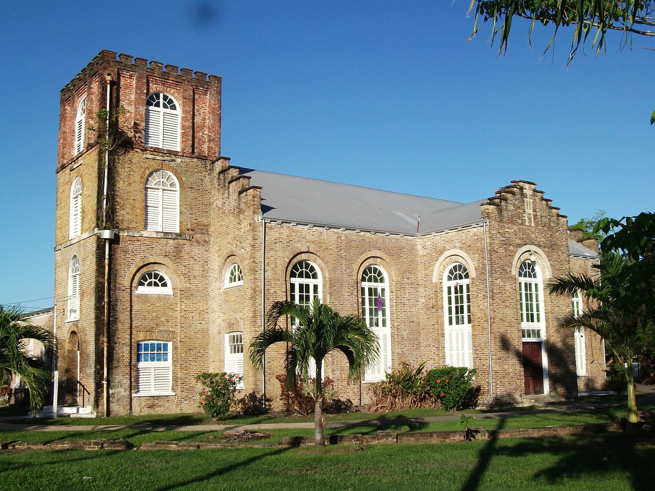 Historic brick church with a bell tower surrounded by palm trees and blue sky.