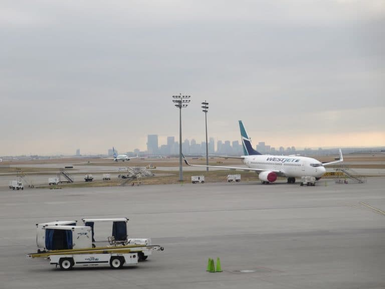 A WestJet airplane is parked on an airport tarmac with a city skyline visible in the background.