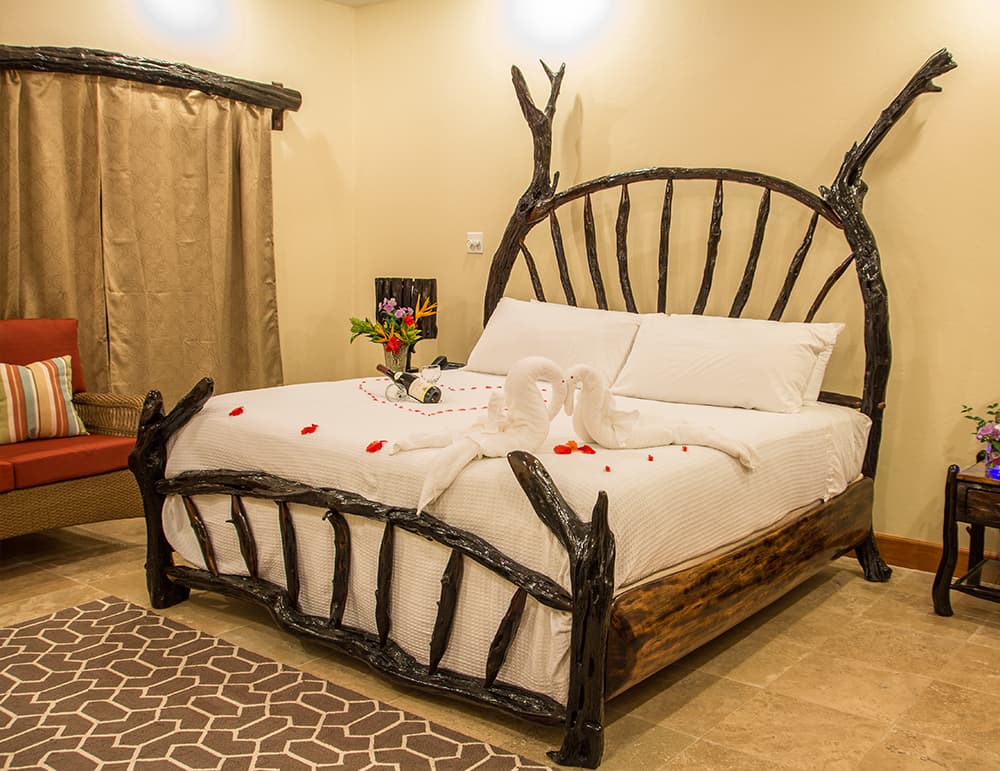 A rustic wooden bed with a unique headboard design and decorative swans made from towels, accented by flowers and rose petals.