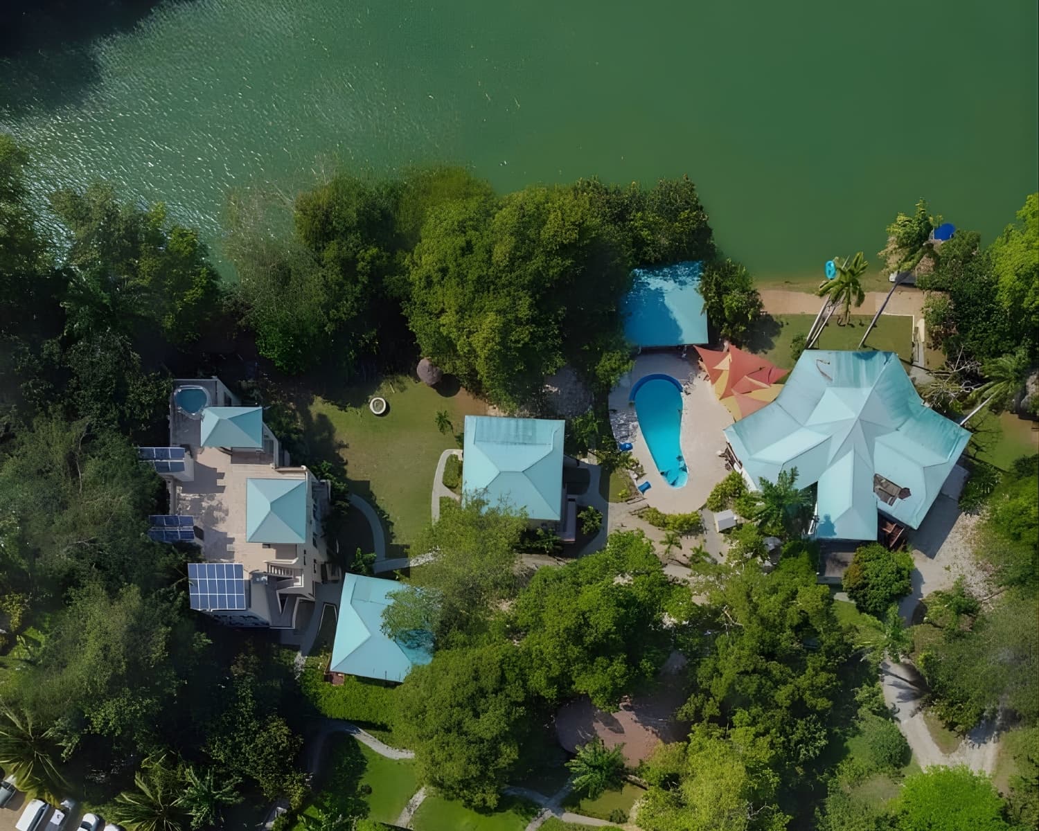 Aerial view of a tropical villa complex with a swimming pool surrounded by greenery and a waterfront.