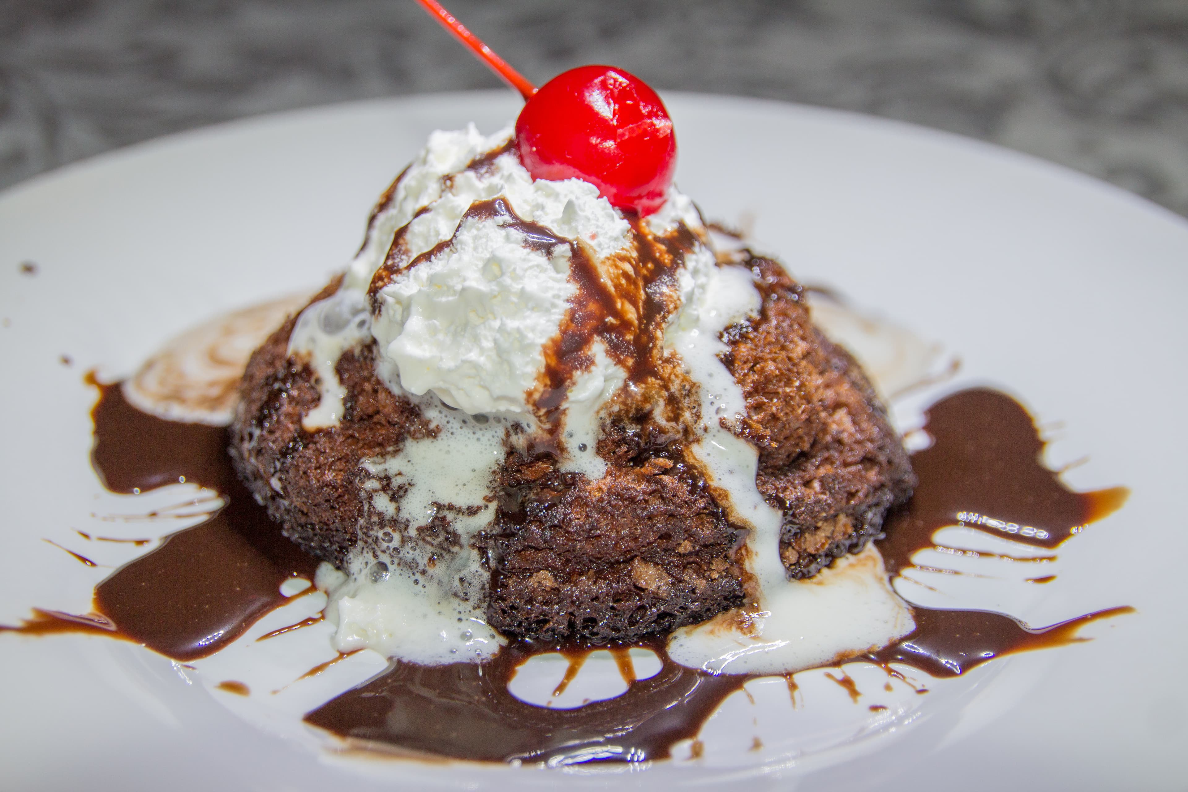 A chocolate dessert topped with whipped cream, a cherry, and drizzled with chocolate sauce.