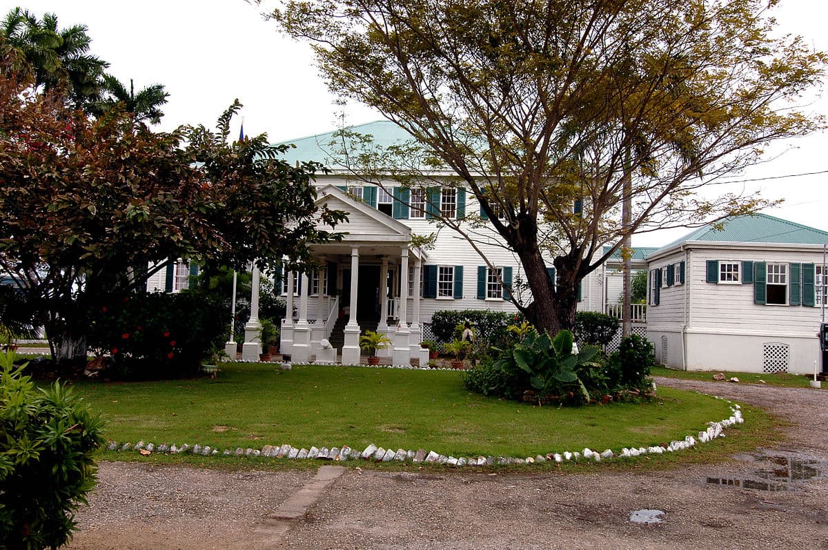 A large white house with a green roof surrounded by a lush garden.
