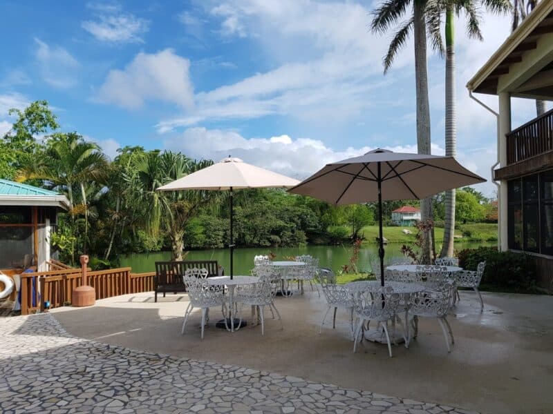 Outdoor seating area with tables and umbrellas overlooking a serene lake and lush greenery.