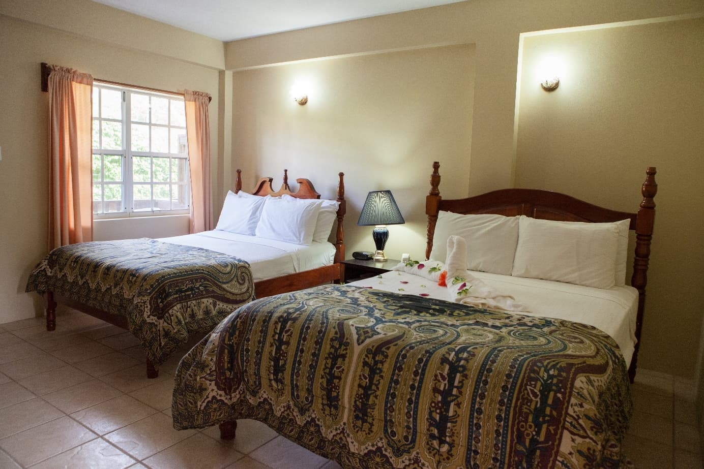 A cozy hotel room featuring two beds with decorative blankets and a window with light curtains.