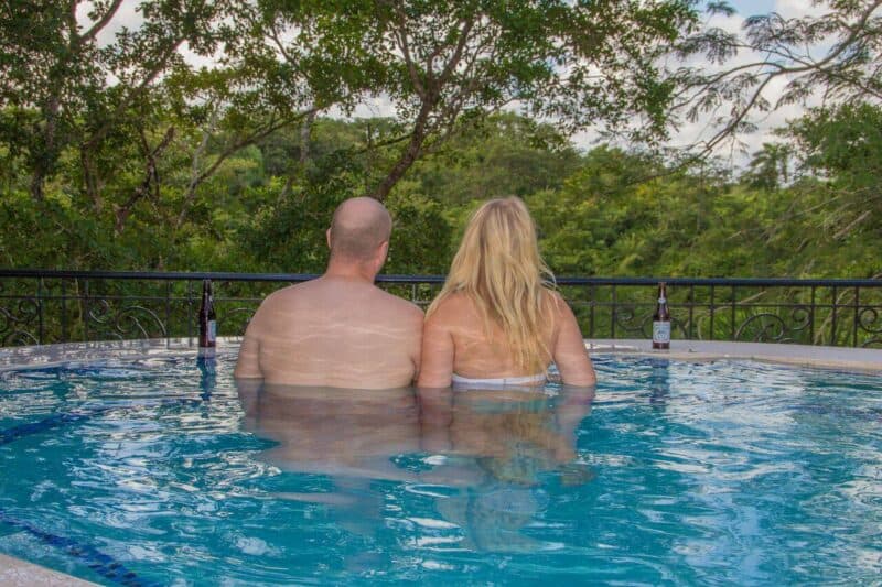 A couple relaxes in a hot tub, overlooking a lush green landscape.