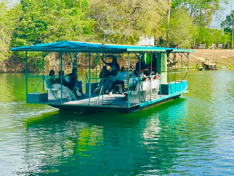A group of people relax on a blue-topped boat floating on calm green water.