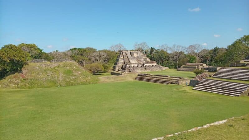 Ancient ruins of a Mayan temple complex surrounded by lush greenery and a blue sky.