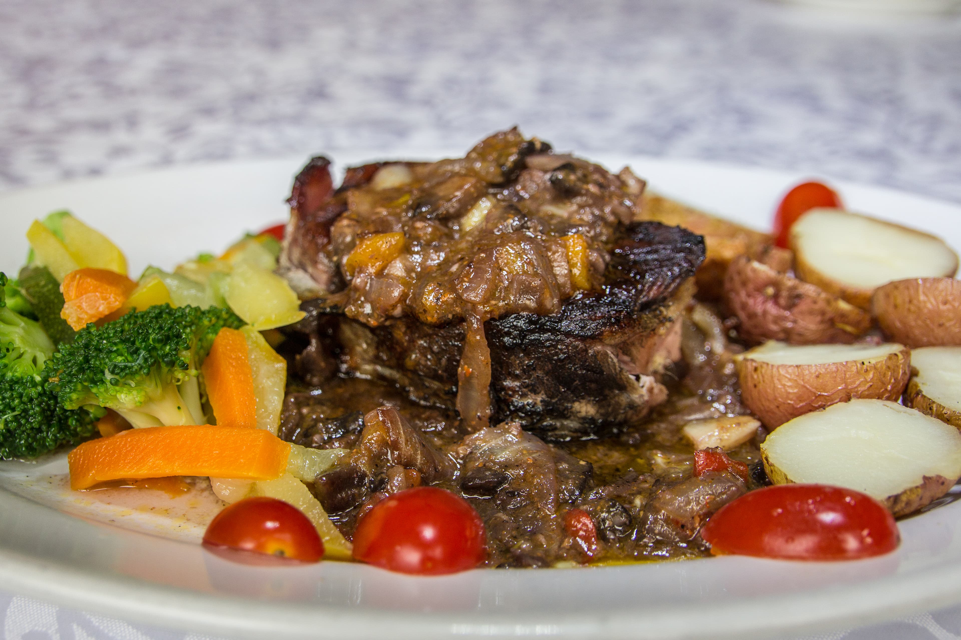 A plate of tender roast beef topped with gravy, served alongside mixed vegetables and baby potatoes.