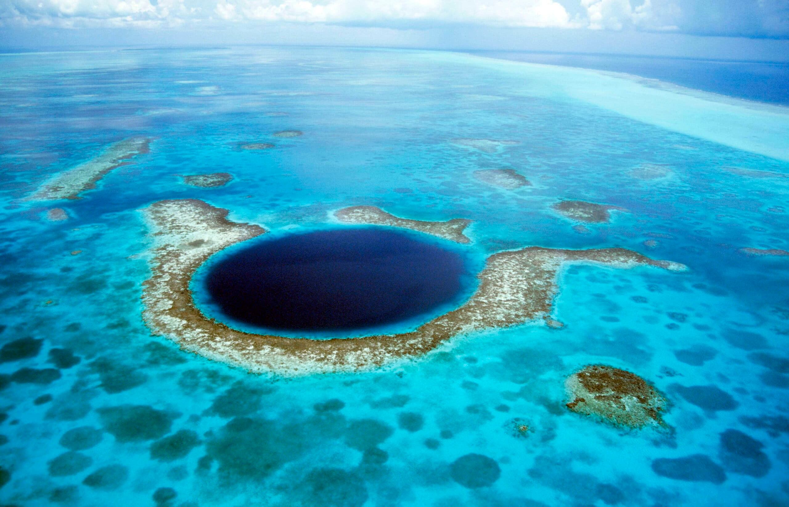 Aerial view of a large circular blue hole surrounded by shallow turquoise waters.