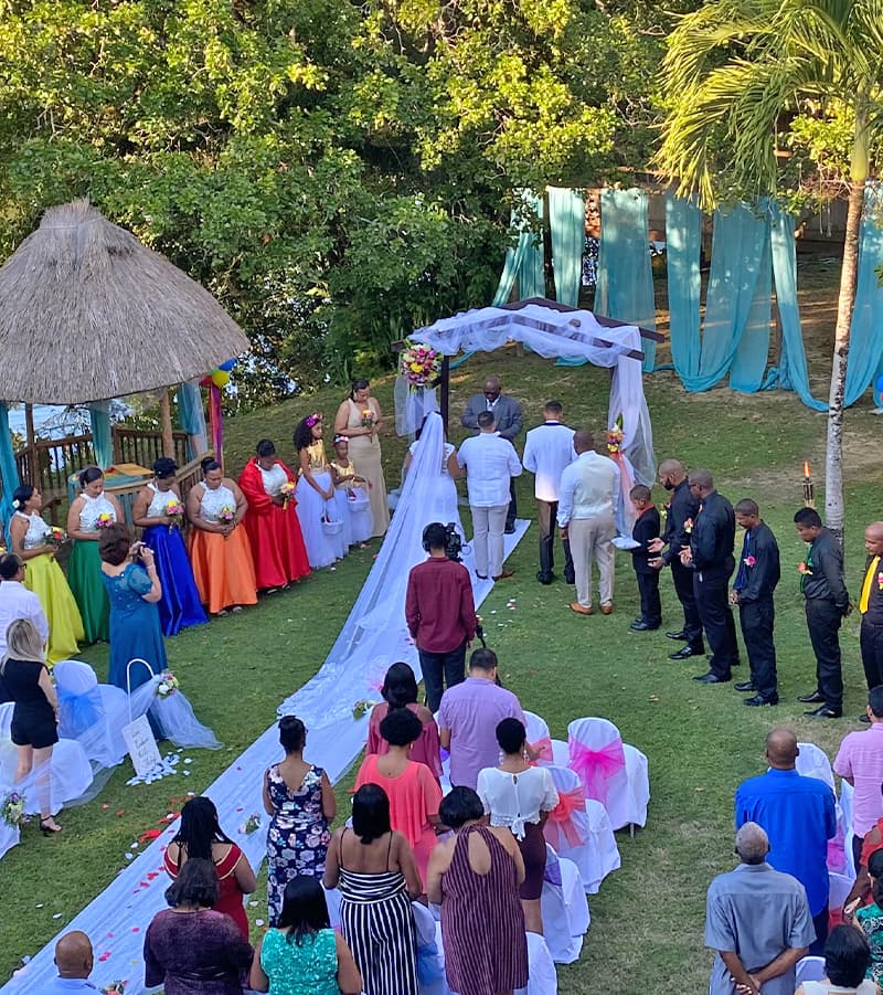 A colorful outdoor wedding ceremony with guests seated and the couple at the altar under a floral arch.