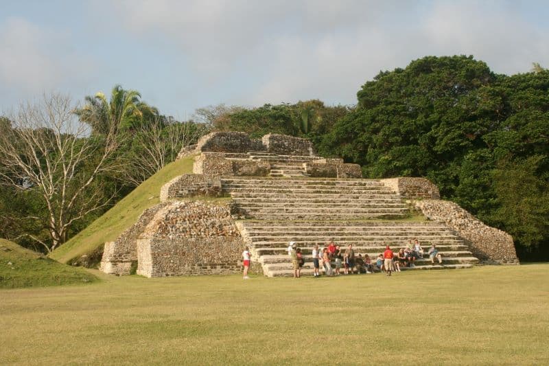 A group of people sits near ancient stone steps surrounded by lush greenery.