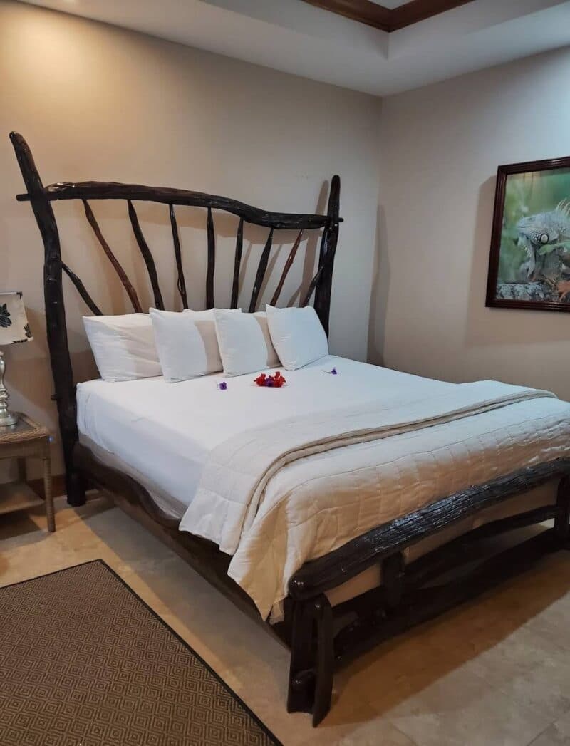 A cozy bedroom featuring a unique wooden bed with decorative pillows and flower petals on the white bedding.