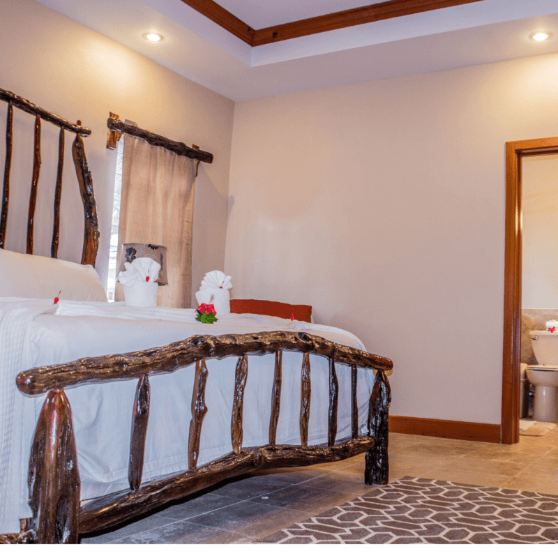 Cozy bedroom featuring a handmade wooden bed, soft linens, and a view of a bathroom through an open door.