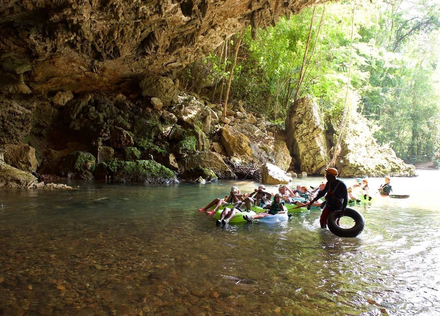 People floating on inner tubes in a serene, cave-like setting surrounded by lush greenery.