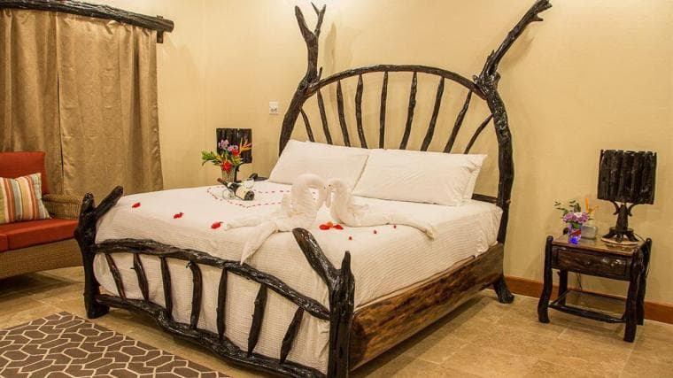 A rustic bedroom featuring a wooden bed with decorative swans and rose petals.