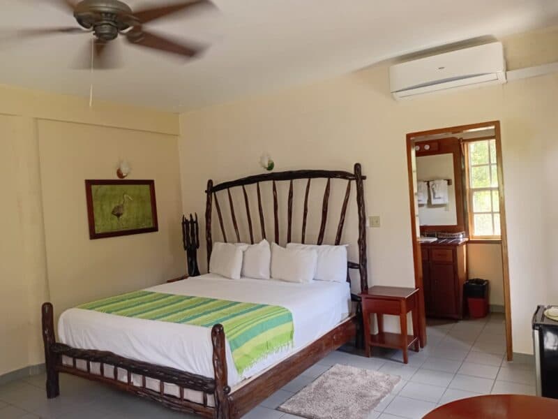 A cozy hotel room featuring a wooden king-size bed, bright white linens, and a small desk by a window.