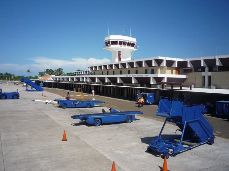 View of an airport terminal with blue ground equipment and a control tower under a clear sky.