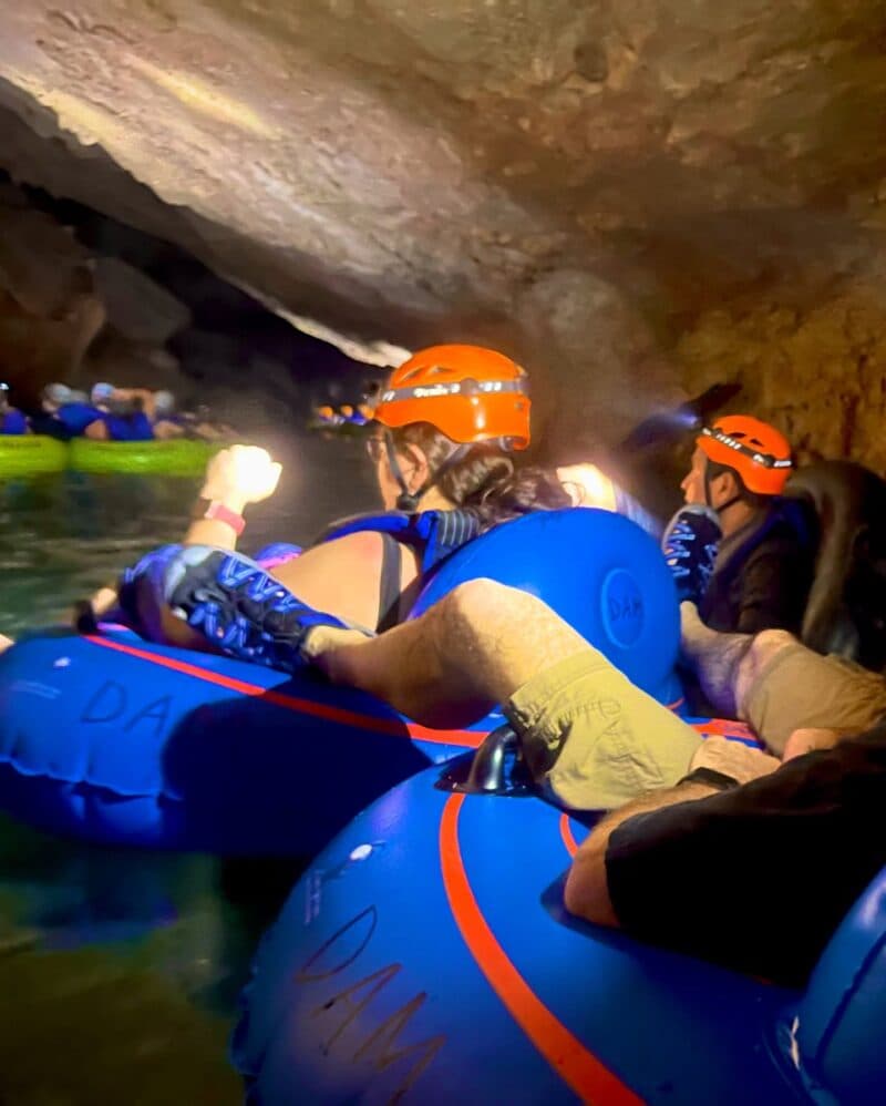 A group of people in blue tubes are navigating a dark cave while wearing helmets.