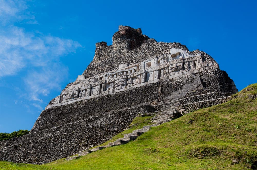 Ancient Mayan temple towering over lush green grass under a clear blue sky.