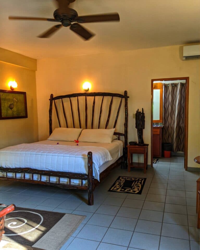 A cozy, well-lit bedroom features a wooden bed, bedside table, and an ensuite bathroom.