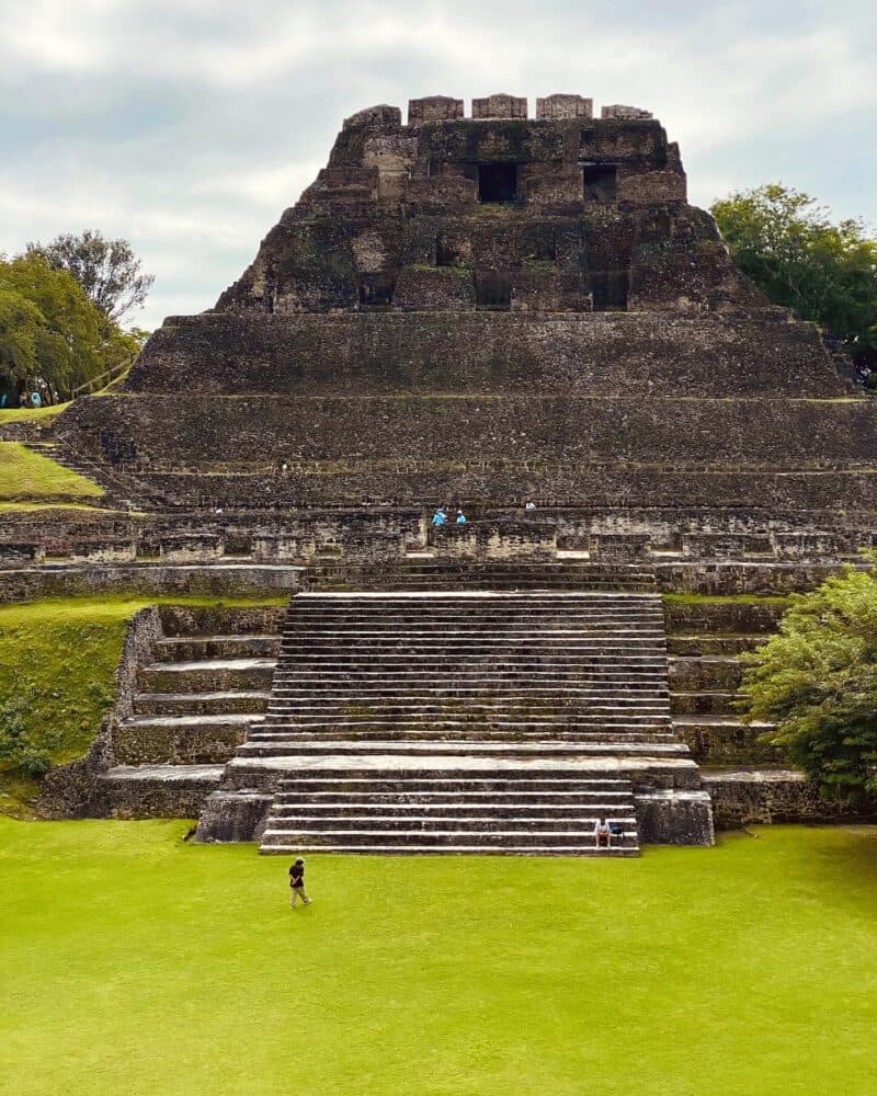 Ancient stone pyramid with steep stairs surrounded by lush green grass and trees.