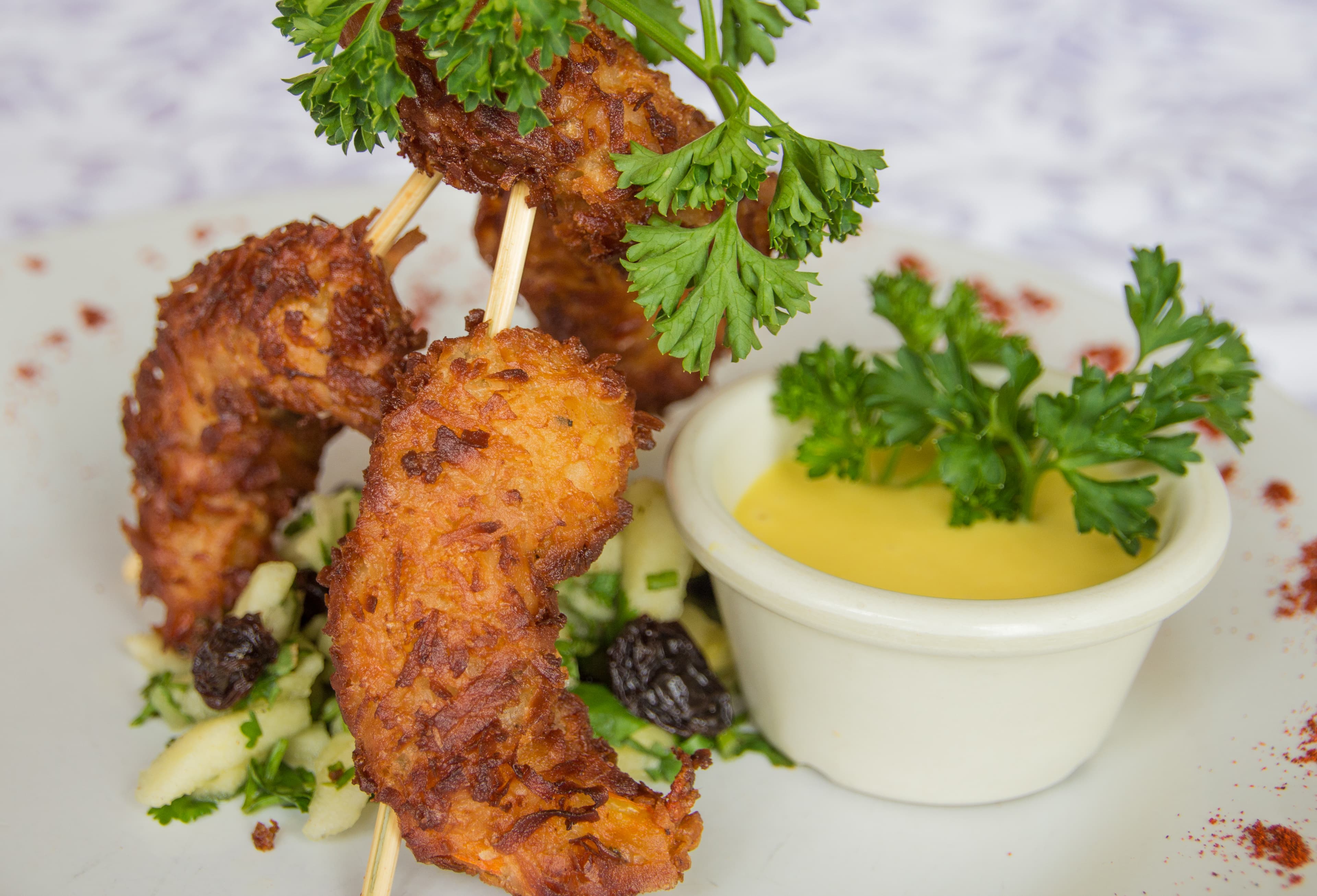 Crispy shrimp skewers garnished with parsley, accompanied by a side of dipping sauce and a fresh salad.