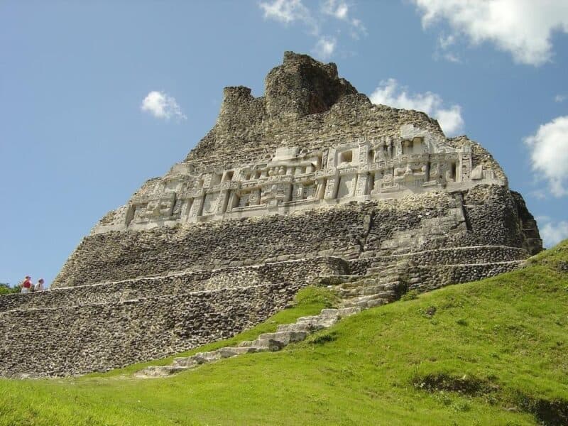 A towering ancient structure partially covered in lush greenery under a bright blue sky.