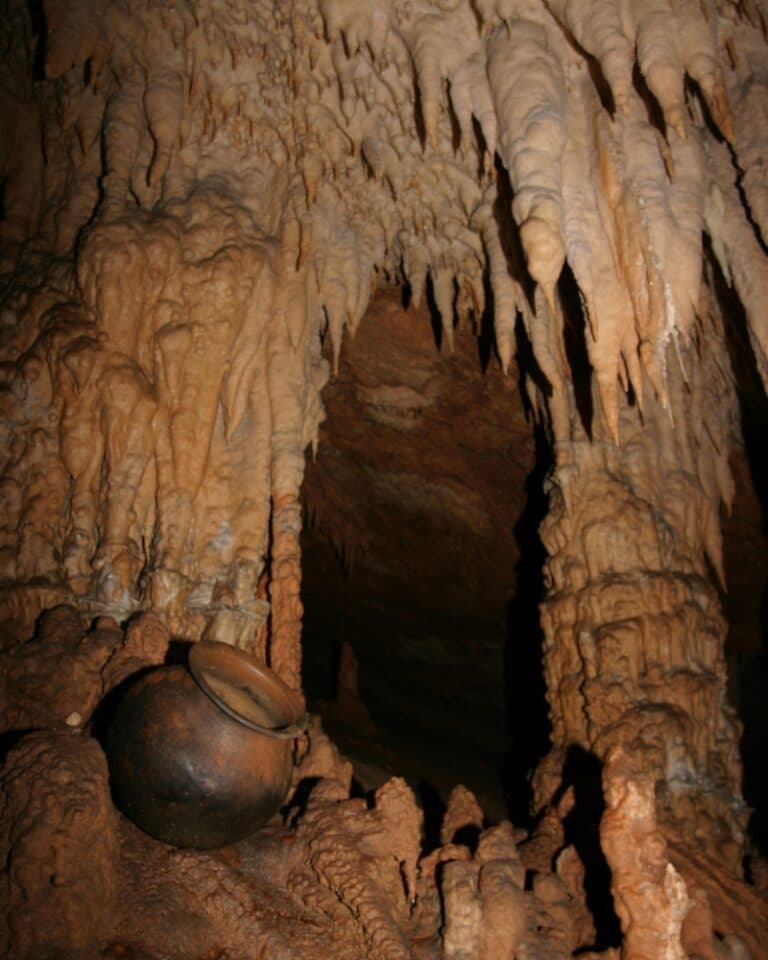 A dark ceramic pot sits among stalactites and stalagmites in a cave.