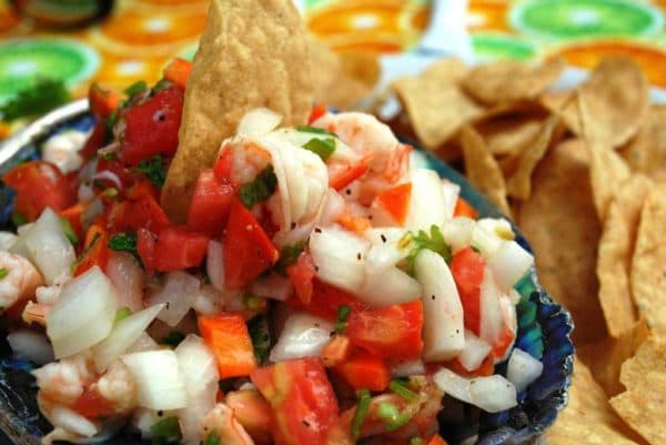 A bowl of shrimp salsa garnished with chopped vegetables and a tortilla chip, surrounded by crispy tortilla chips.