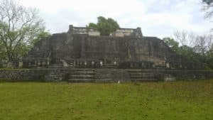Ancient stone pyramid surrounded by greenery under a cloudy sky.