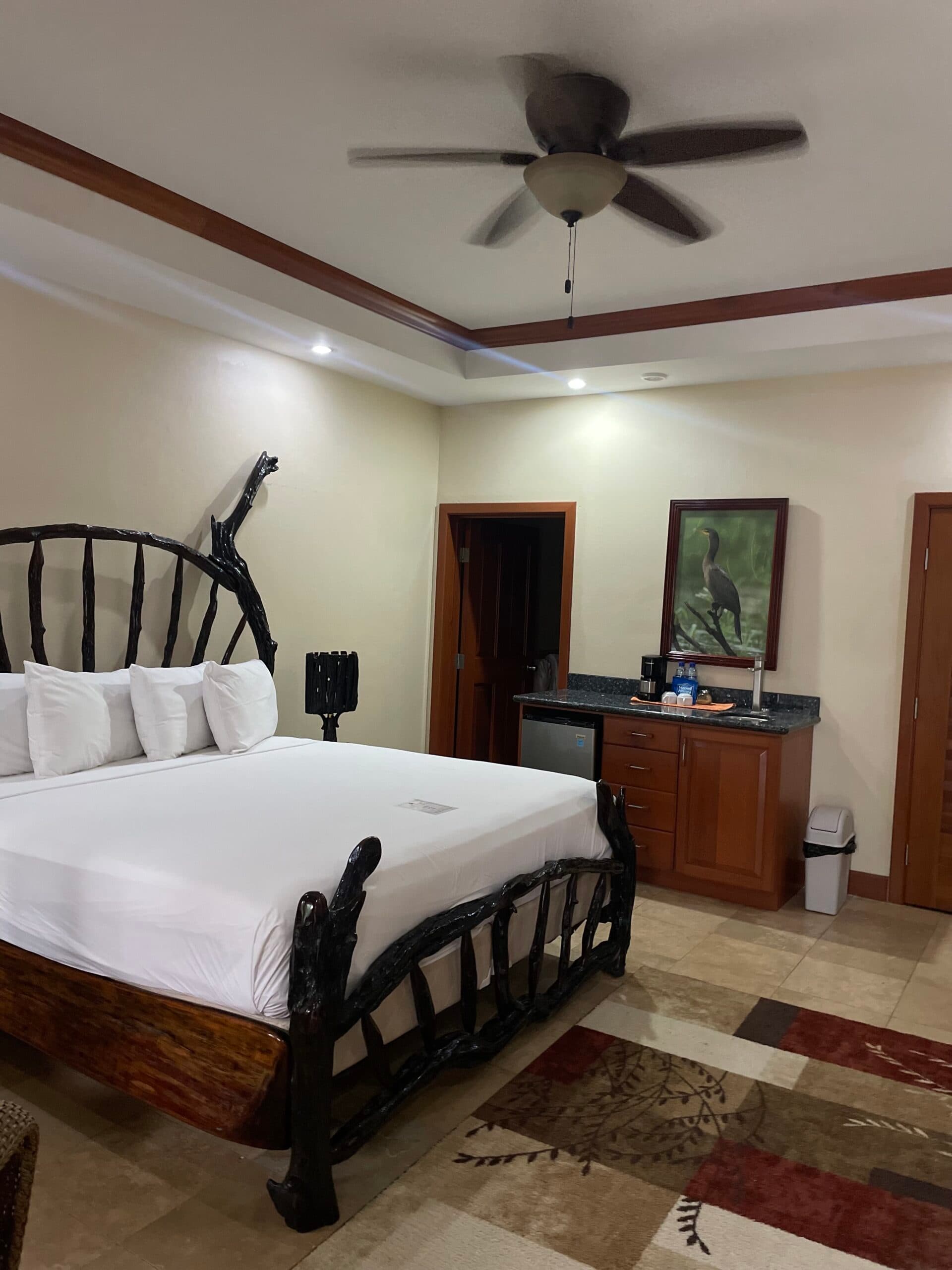 A cozy hotel room featuring a unique wooden bed, a ceiling fan, and a kitchenette area.