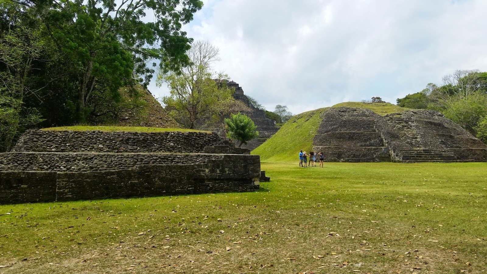 Ancient Mayan ruins surrounded by lush greenery and visitors on a grassy field.