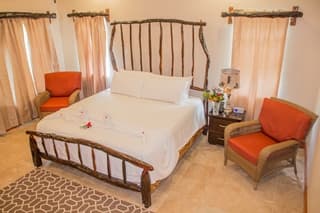 A cozy bedroom featuring a wooden bed, orange accent chairs, and softly draped curtains.
