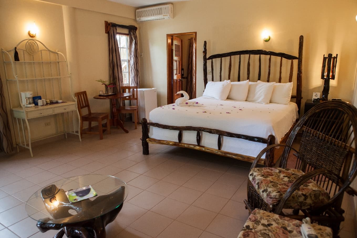 A cozy hotel room featuring a wooden bed, floral armchairs, and a small dining table.
