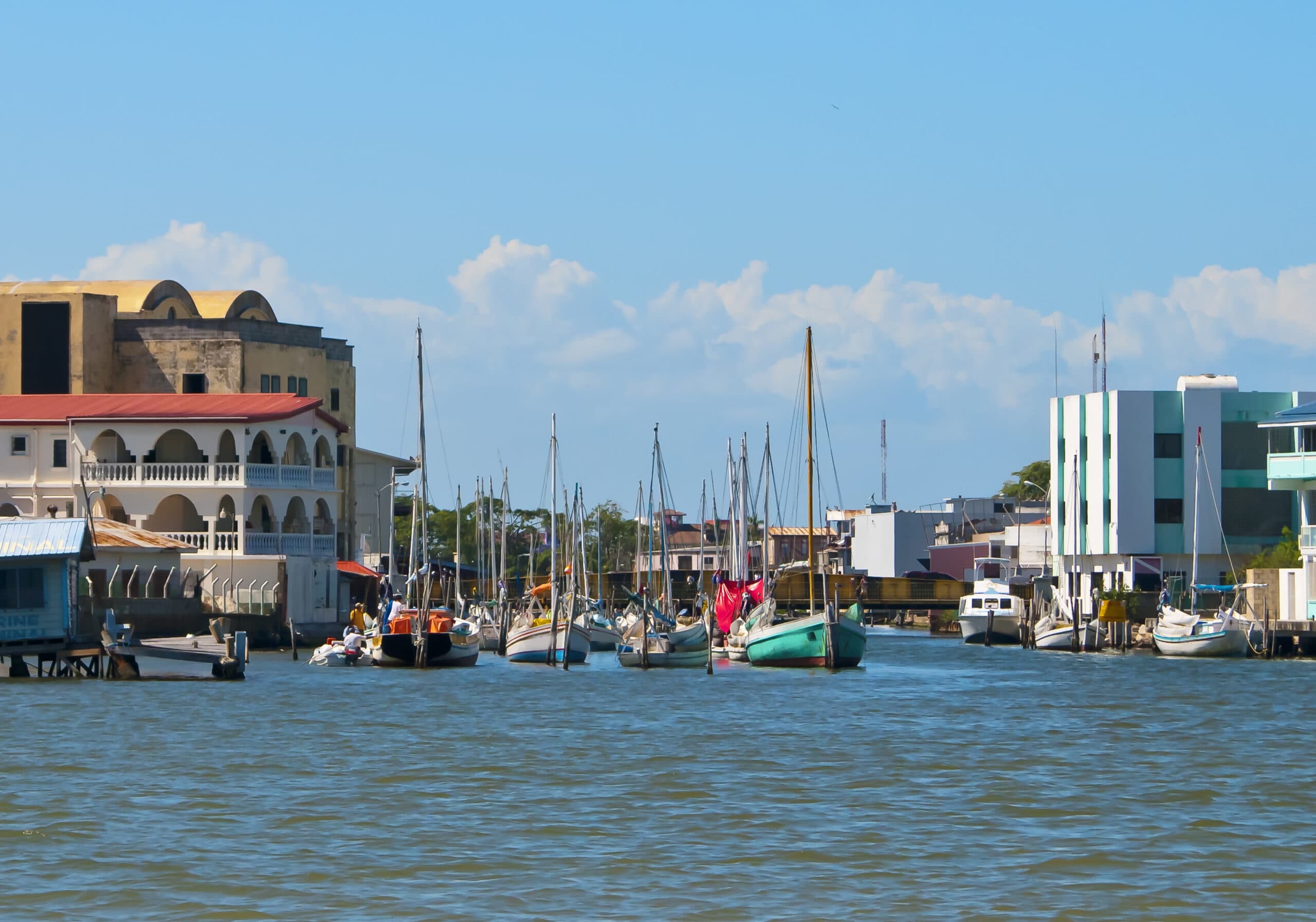A serene harbor scene with various boats docked alongside waterfront buildings under a clear blue sky.