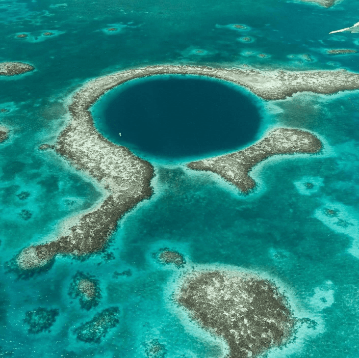 Aerial view of a circular blue hole surrounded by shallow coral reefs in turquoise water.