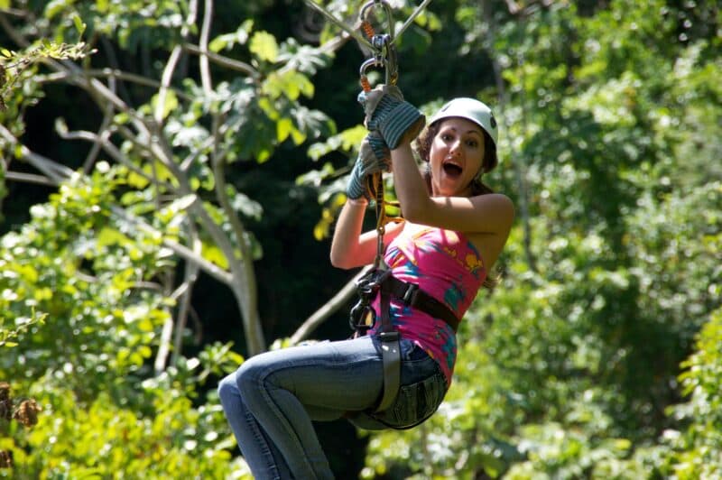 A woman excitedly zip-lining through a lush green forest.