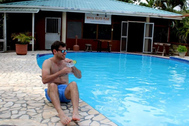 A man sits by a swimming pool, enjoying a drink on a sunny day.