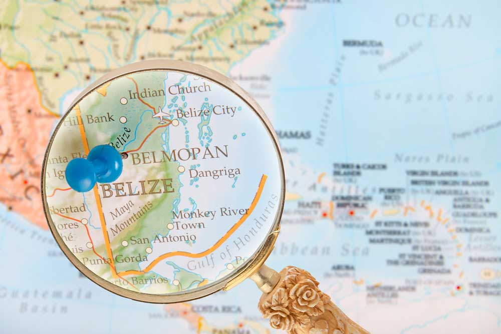 A magnifying glass over a map highlighting Belmopan, Belize, with a blue pin.
