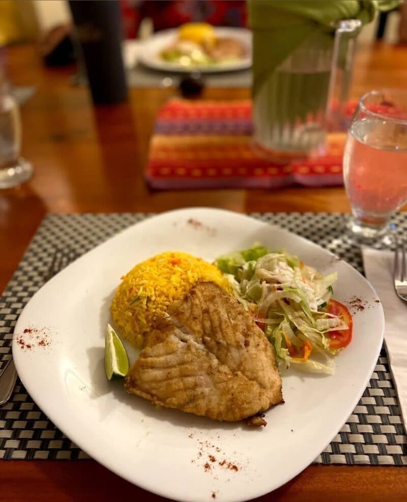 A plate featuring fried fish, yellow rice, salad, and a lime wedge.
