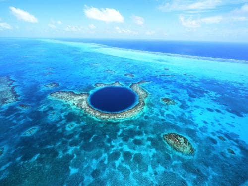 Aerial view of a blue hole surrounded by turquoise waters and coral reefs.