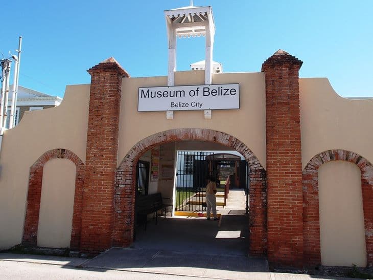 Entrance to the Museum of Belize in Belize City, featuring a white sign and red brick walls.