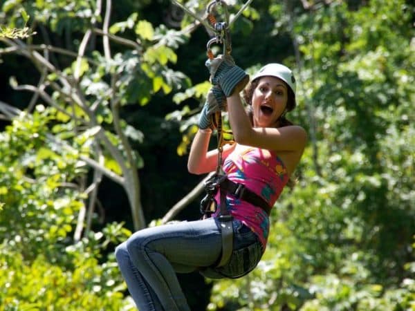 A woman joyfully zip-lining through a lush forest.