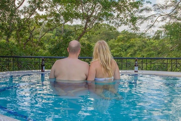 A couple relaxes together in a pool, overlooking a lush green landscape.
