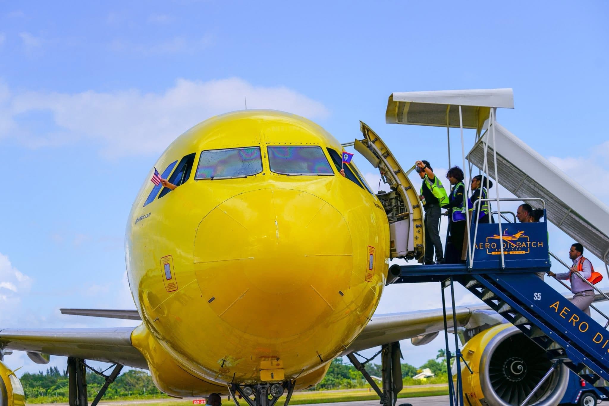 A bright yellow airplane on the tarmac with crew members boarding via a jet bridge.