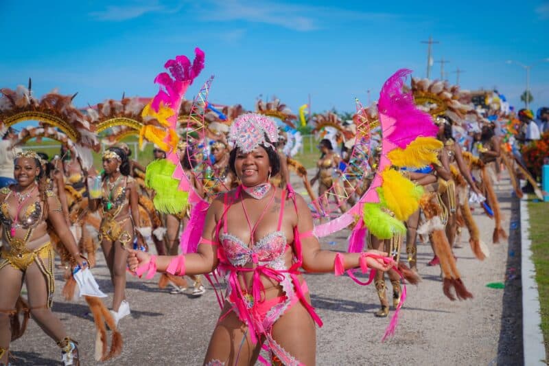 A joyful performer in vibrant pink and feathered costume leads a lively parade.